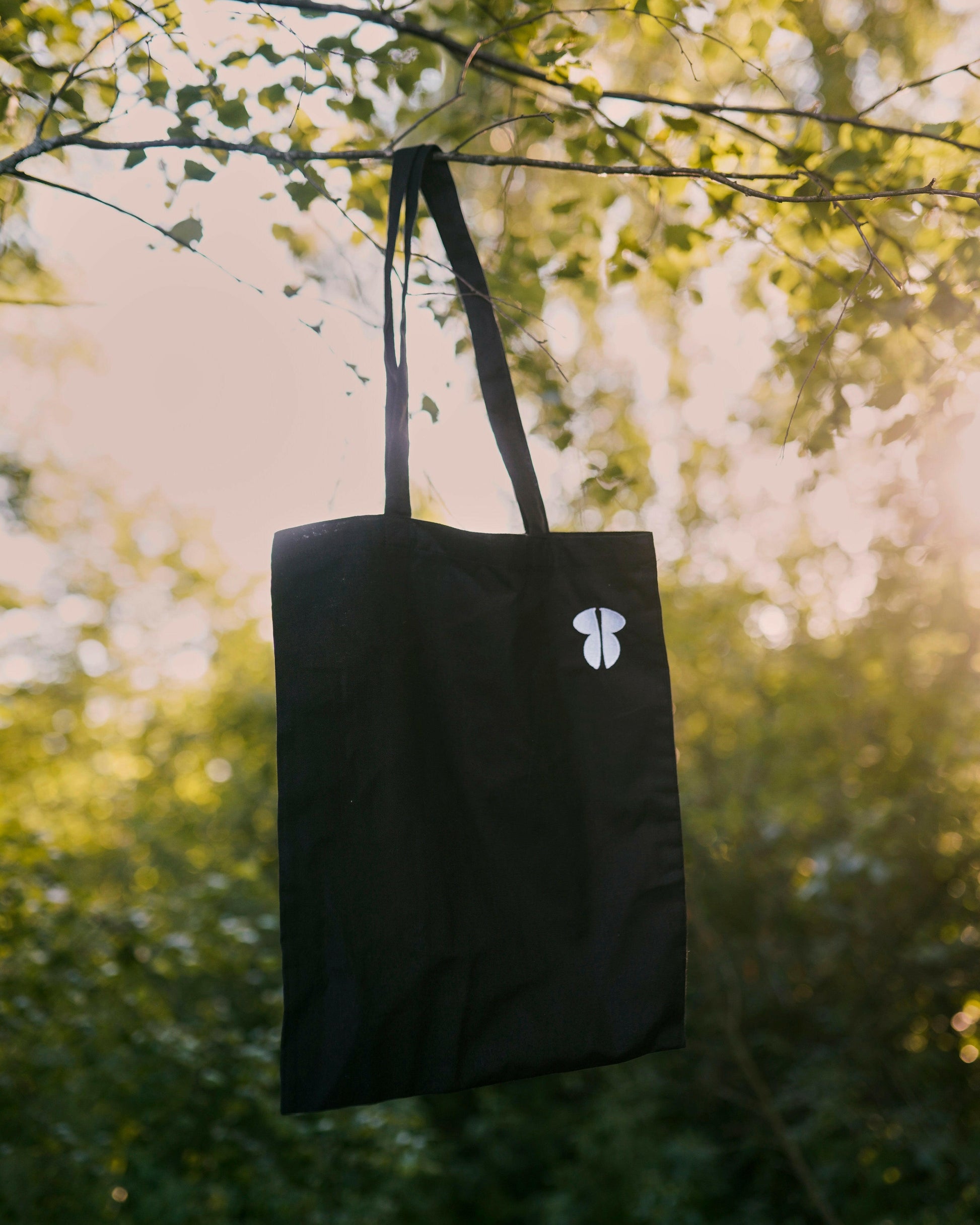 A black eco-friendly tote bag made of organic cotton, featuring the Tropẽle mushroom logo. Stylish, durable, and perfect for everyday use or shopping.